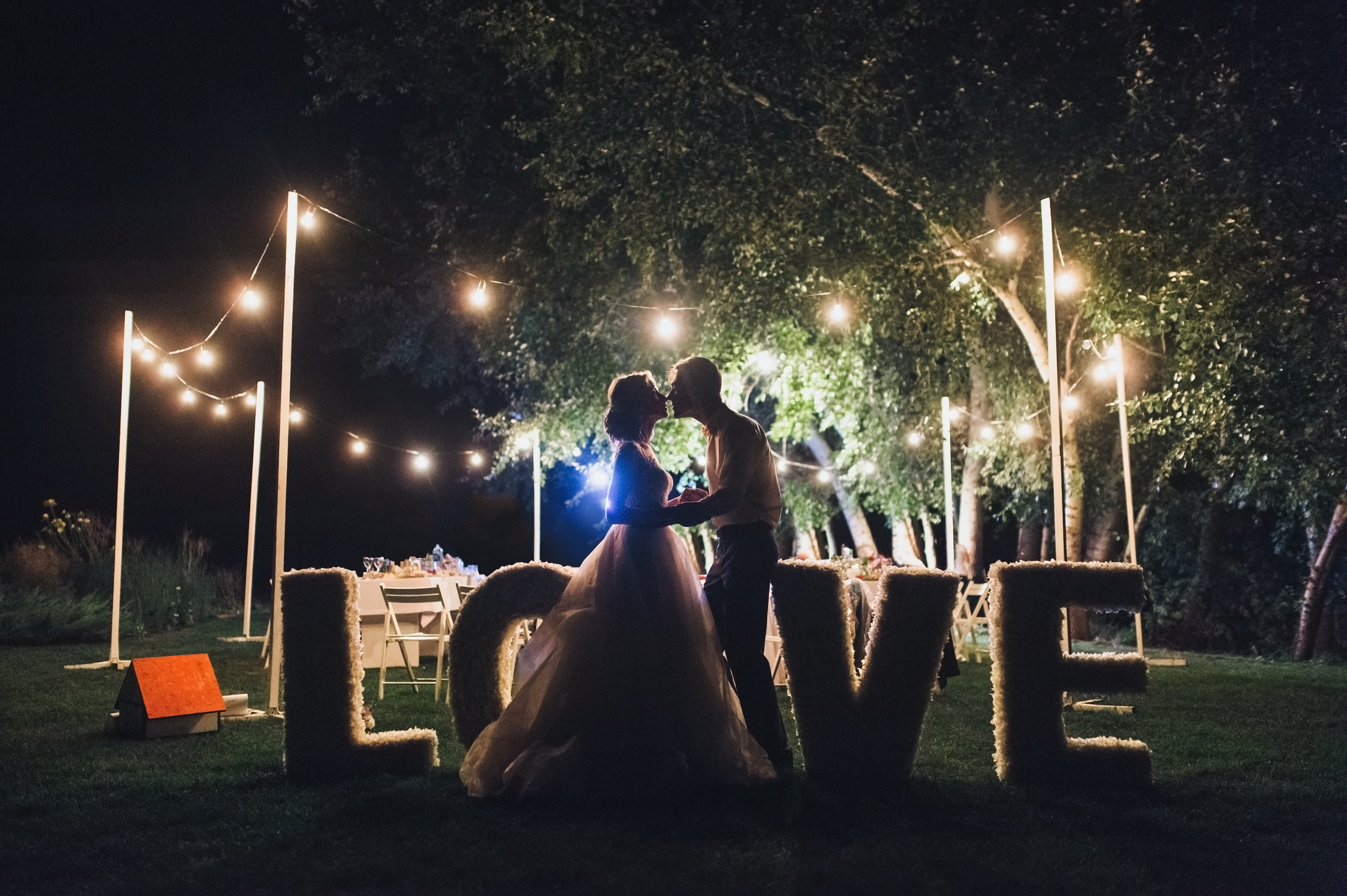 Beautiful newlyweds kiss tenderly at a wedding party with lamps. Stylish wedding ceremony. Love in the frame. Designer letters. Beautiful newlyweds kiss tenderly at a wedding party with lamps. Stylish wedding ceremony. Love in the frame. Designer letters.